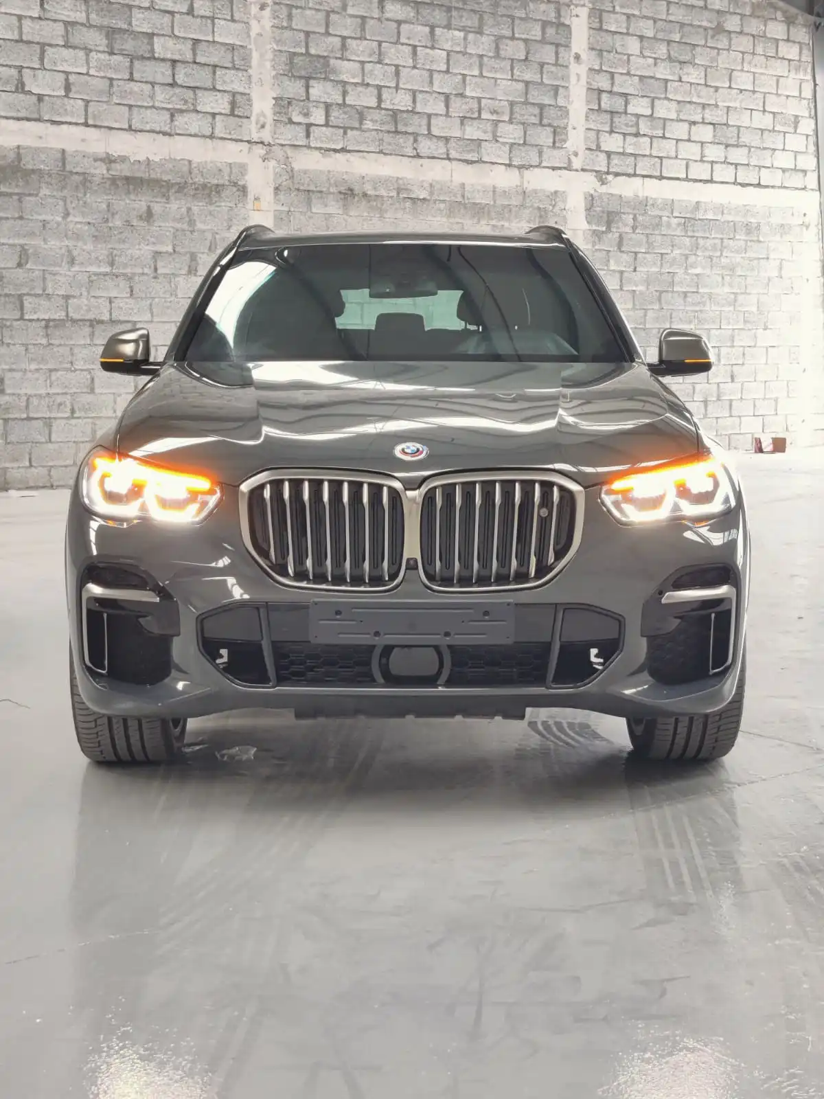 BMW X5 M50i grey armored luxury SUV front view with lights on