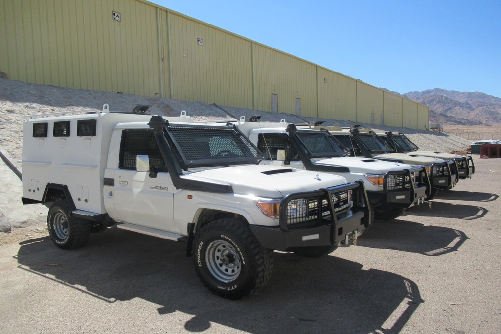 Fleet of Toyota Land Cruiser 70 Series armored security vehicles with protective mesh windshield guards.